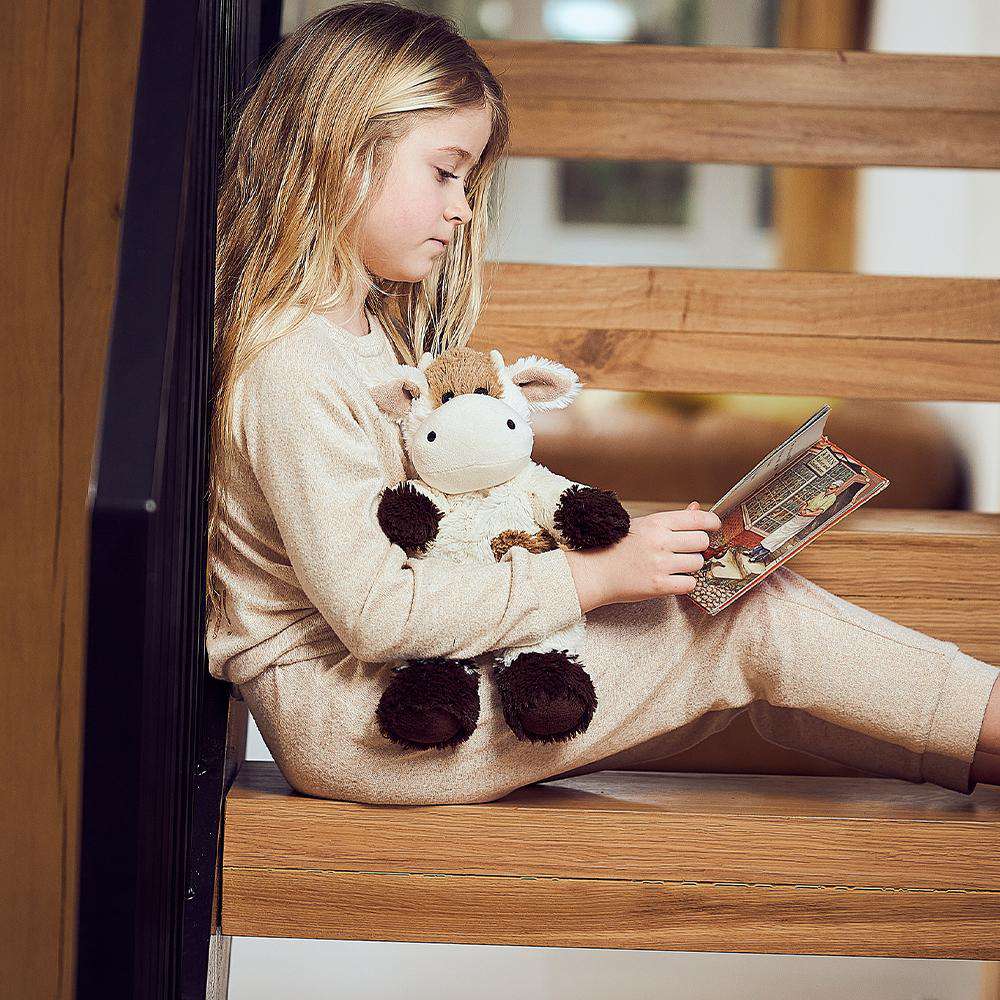 Image 99: Little girl reading a book with Cute Weighted Lavender Scented Cow Stuffed Animal Heating Pad Warmies