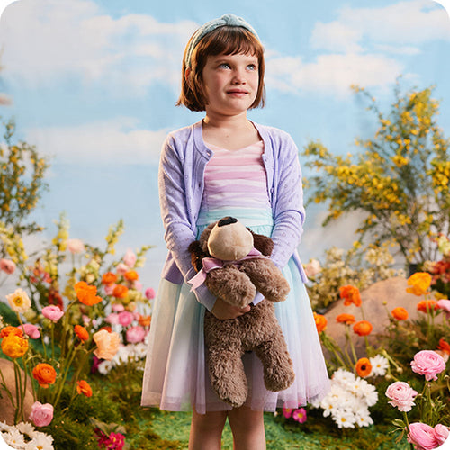 Image 100: girl holding warmies dog stuffed animal in flower field