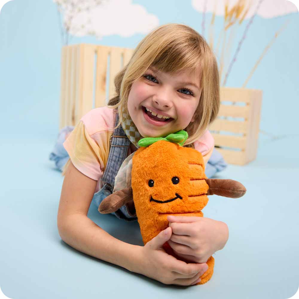 Image 99: Little girl laying flat on the floor while hugging a Carrot Warmies