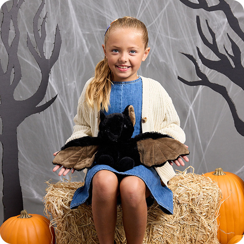 Image 101: girl holding a bat stuffed animal on her lap in a halloween setting