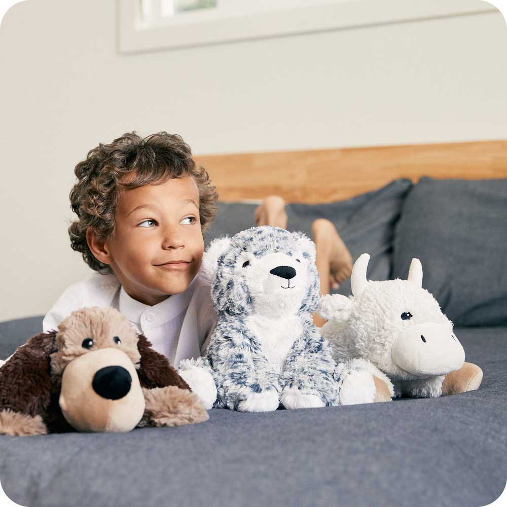 Image 102: Little boy laying down with Soft Warm Weighted Snow Leopard Plush Warmies