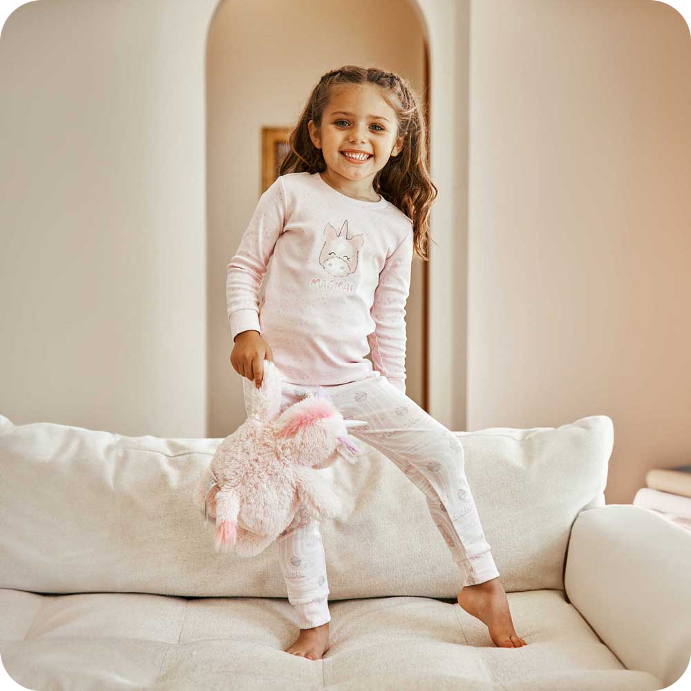Image 86: Child smiling while holding Soft Weighted Warmies Stuffed Animal and wearing Unicorn Pajamas - Warmies USA