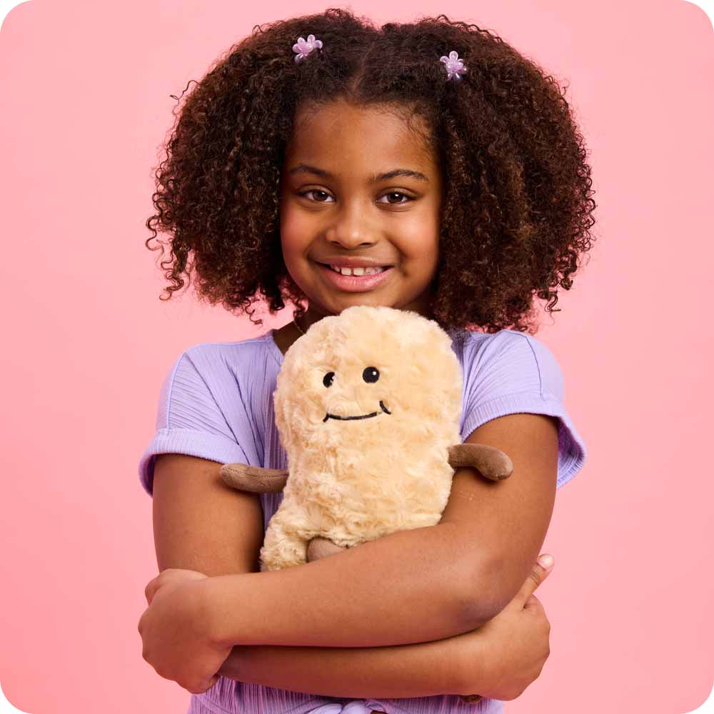Image 101: Peanut Warmies hugged by a little girl in a purple shirt against a pink backdrop.