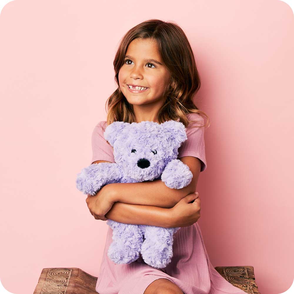 Image 100: Girl smiling and hugging a Cute Weighted Lavender Scented Purple Curly Bear Stuffed Animal Heating Pad Warmies